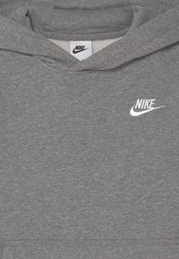 Sudadera gris de Nike con logo bordado en blanco. Tejido suave y texturizado, con capucha y detalle de bolsillo frontal. Diseño simple y deportivo.