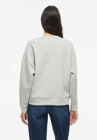 Grå genser med avslappet passform, senkede skuldersømmer, ribbestrikkede mansjetter og kant. Brukes med mørkeblå jeans, som viser et enkelt, avslappet design.