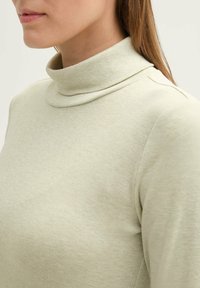 Hellgrüner Rollkragenpullover mit weichem, geripptem Material, figurbetontem Schnitt und umgeschlagenem Kragen. Keine sichtbaren Muster oder Hardware.