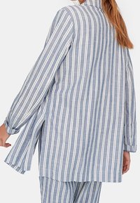 Modrobíle pruhovaná dlouhá košile z lehké látky; má dlouhé rukávy, boční rozparky a volný střih.