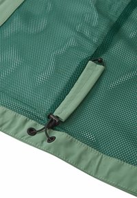 Tissu en maille verte avec une bordure lisse et unie. Dispose d'une fermeture à cordon de serrage et d'une surface texturée avec de petits trous pour la ventilation.