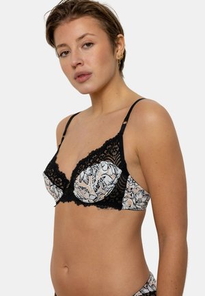 Bralette en dentelle avec des bonnets à motif floral en blanc et noir. Dispose de bretelles réglables et de détails en dentelle sophistiqués le long des bords.