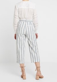 Witte blouse met kantdetails, gecombineerd met lichtblauwe en witte verticaal gestreepte culottes. Beige blockhakken met een strik maken de outfit compleet.