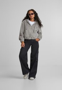 Grå, fuzzy cropped hættejakke med elastiske manchetter, parret med højtsiddende mørk denim cargobukser med sidelommer og frynsede kanter.