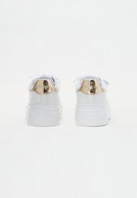 Sneaker bianche con suola spessa, caratterizzate da un cappuccio del tallone in oro metallico con il nome del marchio impresso. Lacci e colletto imbottito in bianco abbinato.