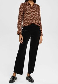 Chemise à manches longues à motifs dans des tons chauds de marron et d'orange, associée à un pantalon en velours noir taille haute et des mocassins noirs brillants.