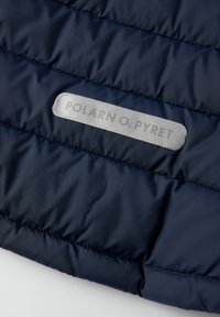 Mørkeblå quiltet stof med vandrette syninger og et refleksivt rektangulært label med teksten "POLARN O. PYRET."