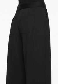 Black high-waisted trousers with a smooth fabric, wide leg, and two back pockets featuring stitched detailing.