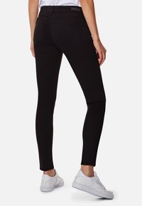 Los jeans negros de corte ajustado presentan una textura suave, un cinturón de cintura media y bolsillos traseros. Combinados con zapatillas blancas.