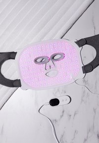 LED-ansiktsmask i vit silikon med rosa ljusgaller, har utskärningar för ögonen, justerbara svarta remmar och en vit fjärrkontroll.