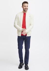 Lys cremet zip-up jakke med tekstureret mønster, rød crew neck t-shirt, marineblå bukser og sorte sko. Casual og moderne outfit arrangement.