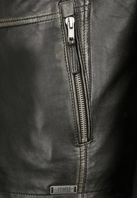 Sektion av svart läderjacka med en framträdande silverdragkedja och sömnadsdetaljer. Texturerat material med en matt finish.