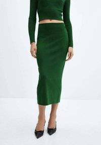 Haut en tricot côtelé vert et jupe midi assortie. Le tissu est lisse avec une silhouette ajustée, complété par des escarpins noirs à talons pointus.
