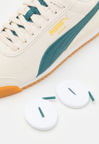 Sneaker beige in suede con dettagli in turchese, marchio in oro e suola in gomma arancione. Include due paia di lacci bianchi con punte turchesi.