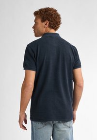 Tricou polo bleumarin din material texturat, cu mâneci scurte și guler clasic, asortat cu blugi din denim de un bleu deschis.