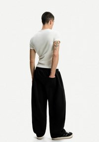 Bílá přiléhavá košile s krátkým rukávem spárovaná s volnými černými kalhotami s elastickým pasem a boční kapsou. Černé tenisky dokreslují celý vzhled.