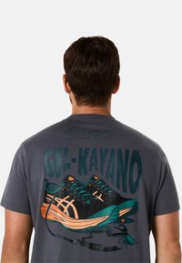 Grå bomulds t-shirt med et grafik af ASICS Gel-Kayano sko i sort og teal med orange detaljer. Inkluderer teksten "GEL-KAYANO" i fed skrift.