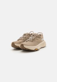 Beige trail shoes with textured upper, reinforced toe, and cushioned sole. Features Vibram outsole and elastic laces for secure fit.