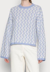 Maglione blu chiaro con motivo a zigzag bianco, colletto rotondo, maniche lunghe e polsini e orlo a coste. Texture morbida, design cropped.