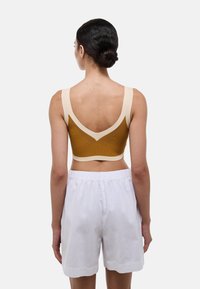 Soutien-gorge de sport marron et crème avec un design en V, texture côtelée, bretelles larges, associé à un short blanc. Vue arrière présentée.