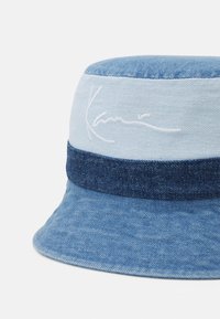 Blå denim bøttehatt med en lysere blå bånd og hvit brodert signatur. Myk tekstur med en bred, fleksibel brem.