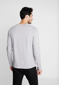 Long-sleeve gray t-shirt in cotton blend, featuring a crew neck and relaxed fit. Worn with black pants, showing the back view.