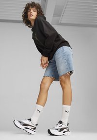 Felpa nera con una grafica colorata, pantaloni corti in denim azzurro chiaro, calzini sportivi bianchi e sneaker bianco-neri con un design distintivo.