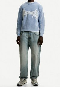 Ljusblå stickad tröja med vitt grafiskt mönster, i kombination med löst sittande ljusblå jeans och grå sneakers.