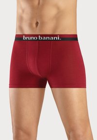 Röda bomullskalsonger med svart elastisk midja som har vit "bruno banani"-logotyp. Slät textur och figurnära design.