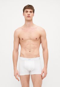 Boxer-culottes blanches en coton avec une ceinture douce affichant "GAP". Le tissu est lisse, avec une coupe ajustée et sans motifs supplémentaires.