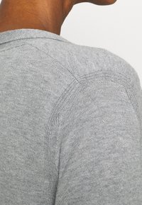 Grau gestrickter Pullover mit rundem Ausschnitt, sichtbaren Nähten und gerippten Akzenten am Kragen und an den Schultern. Weiche Textur.