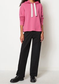 Roze hoodie met contrasterende witte koorden, gecombineerd met zwarte wijde broek en chunky zwarte schoenen. Glad weefsel.