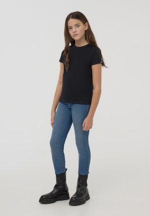 Maglietta nera a maniche corte, abbinata a jeans skinny blu e stivali neri alla caviglia. La maglietta ha un design semplice senza pattern.