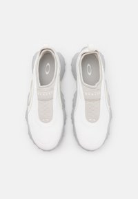 Baskets blanches au style sportif avec un dessus texturé, des accents gris, une conception élastique à enfiler, et une semelle en caoutchouc épaisse. Logos sur la languette et sur le côté.