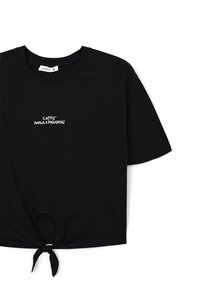 Czarny bawełniany t-shirt z krótkim rękawem i węzłem na dole. Na przodzie znajduje się biały napis "CAFFE ANSIA & PARANOIE".