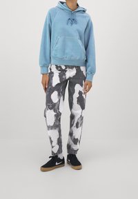 Felpa con cappuccio azzurro chiaro con tasca frontale, abbinata a jeans nero e bianco tie-dye e sneakers nere con suola in gomma.