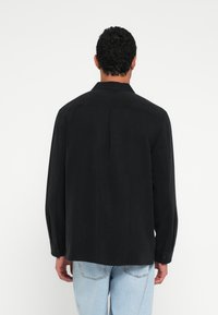 Musta pitkähihainen paita, jossa on suora leikkaus, pehmeä tekstuuri ja takana olkasauma, yhdistetty vaaleansinisiin farkkuihin.