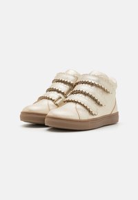 Guldmetalliska sneakers med tre vågformade kardborreband, rund tå och en texturerad brun gummisula. Avslappnad design som passar för vardagsbruk.
