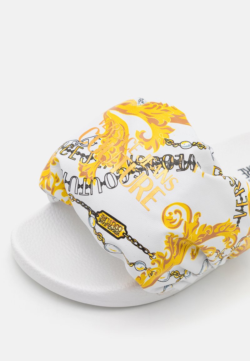 Witte slidesandal met een gevoerde band met een gouden en zwart ornamenteel patroon en gedrukte tekst. Getextureerde, witte rubberen zool.