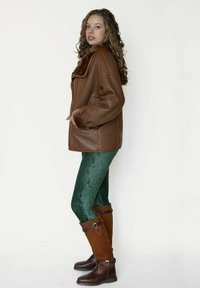 Bruine leren jas met een brede kraag en bontvoering, gecombineerd met groene fluwelen legging en bruine kniehoge laarzen met gespen.