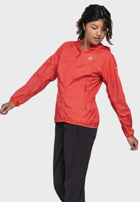 Rote leichte Jacke mit Kapuze, ausgestattet mit einem Frontreißverschluss, elastischen Bündchen und zwei seitlichen Reißverschlusstaschen. Glattes, wasserabweisendes Material.