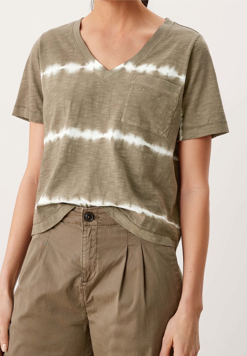 Olivově zelený top s krátkým rukávem ve tvaru V se bílými pruhy tie-dye, s kapsou na prsou a volným střihem, kombinovaný s khaki kalhotami.