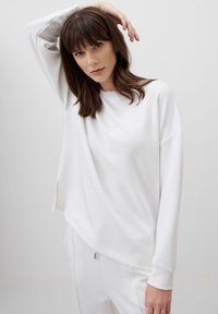Felpa bianca oversized in un tessuto morbido, con scollo rotondo e spalle abbassate. Le fessure laterali aggiungono un dettaglio di design rilassato.