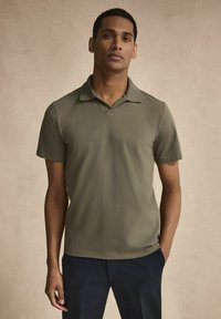 Olivgrön polo skjorta med krage, korta ärmar och en mjuk textur. Skjortan har en ren design med minimal detaljering.