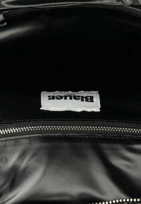 Interno di una borsa nera con zip, caratterizzato da una superficie liscia. Un'etichetta bianca con la scritta "Blauer" stampata in nero è visibile all'interno.