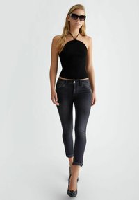 Top negro de canalé con tirantes halter, jeans skinny de mezclilla oscura con sutiles embellishments, y tacones negros de punta. Modelo con gafas de sol oversized.