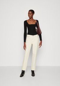 Haut à manches longues noir côtelé avec décolleté carré, associé à un jean droit crème et des bottines noires; tenant un sac à bandoulière bordeaux.