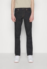 Donkerdenim jeans met een rechte snit, voorzien van oranje stiksels en zakken. Gecombineerd met witte sneakers en een beige top.