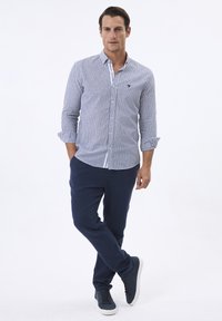 Camisa de manga larga a rayas azul y blanca, de diseño abotonado, con un cuello azul sólido. Combinada con pantalones marinos y zapatillas oscuras.