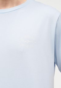 Ανοιχτό μπλε κοντομάνικο t-shirt με αχνό λευκό λογότυπο Pepe Jeans και κυκλικό κείμενο στην αριστερή πλευρά του στήθους.